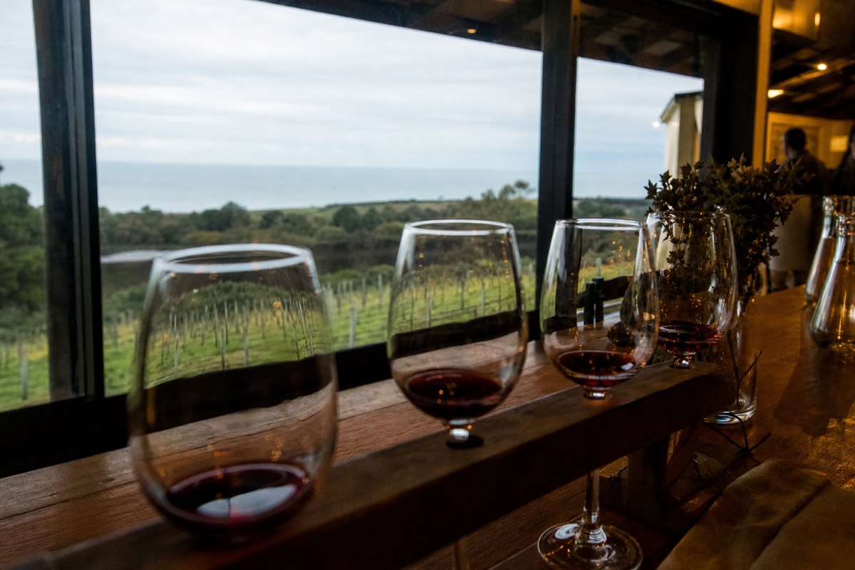 Pinot noir glasses on a rail above a Mornington Peninsula vineyard with the sea beyond
