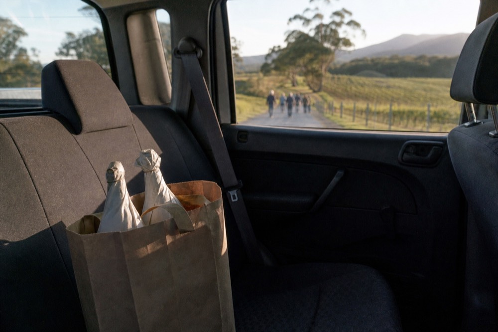 Two wrapped wine bottles in a paper carry bag sitting on the back seat of a tour van