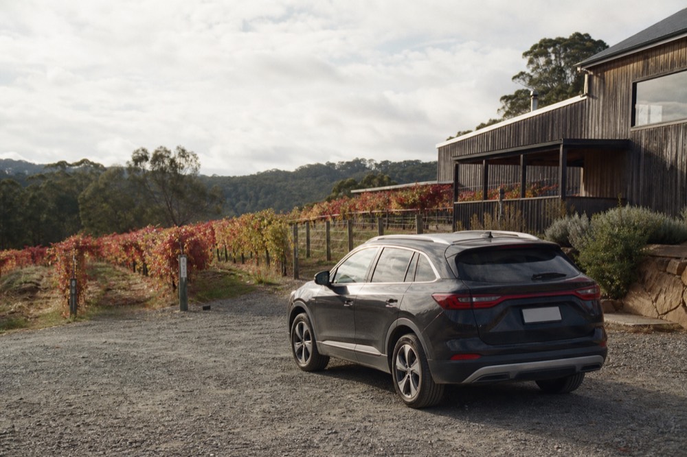 Hire car parked on gravel outside a small rural cellar door with vines running up the slope behind